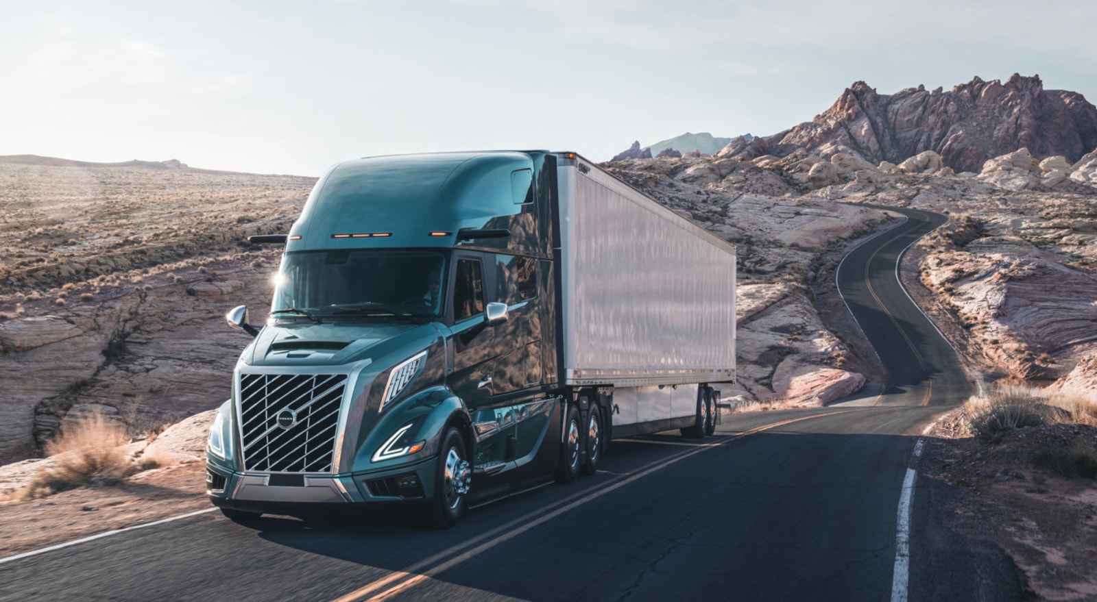 A semi-truck hauling a trailer on a winding road through rocky desert landscape
